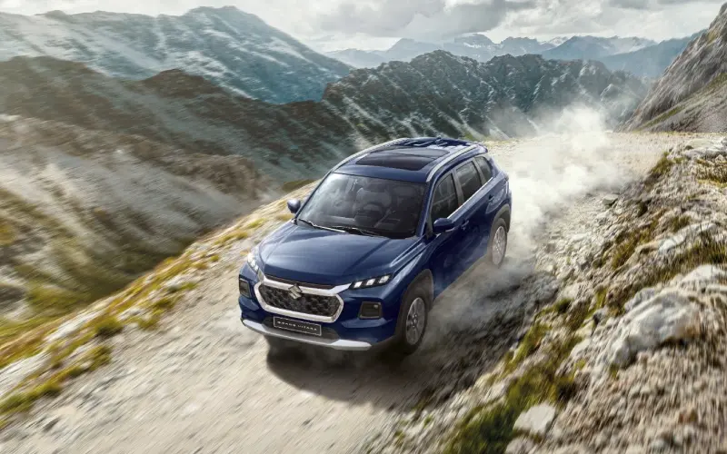 Suzuki Grand Vitara Híbrido azul conduciendo por un camino montañoso polvoriento.